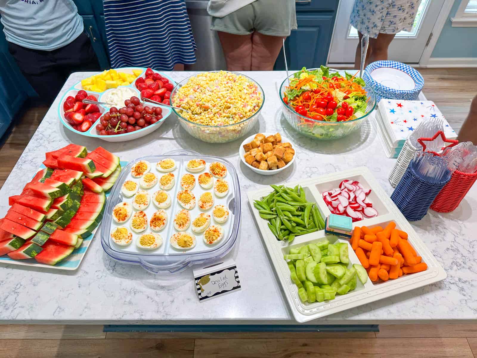The kitchen island is filled with fresh fruits and vegetables and deviled egg platters for the party.