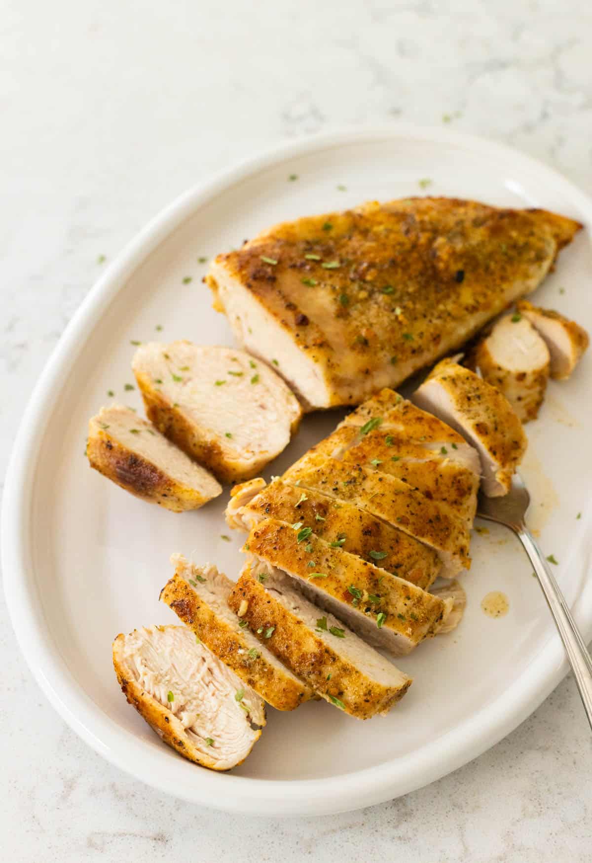 Two sliced oven baked chicken breast halves are served on a white platter.