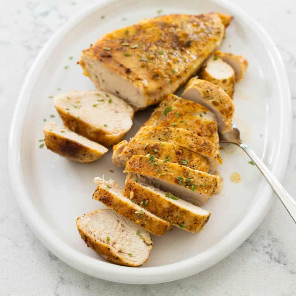 Two sliced oven baked chicken breast halves are served on a white platter.
