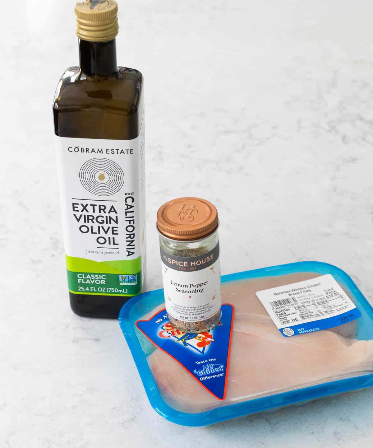 The bottle of olive oil, package of chicken, and seasonings are on the counter.