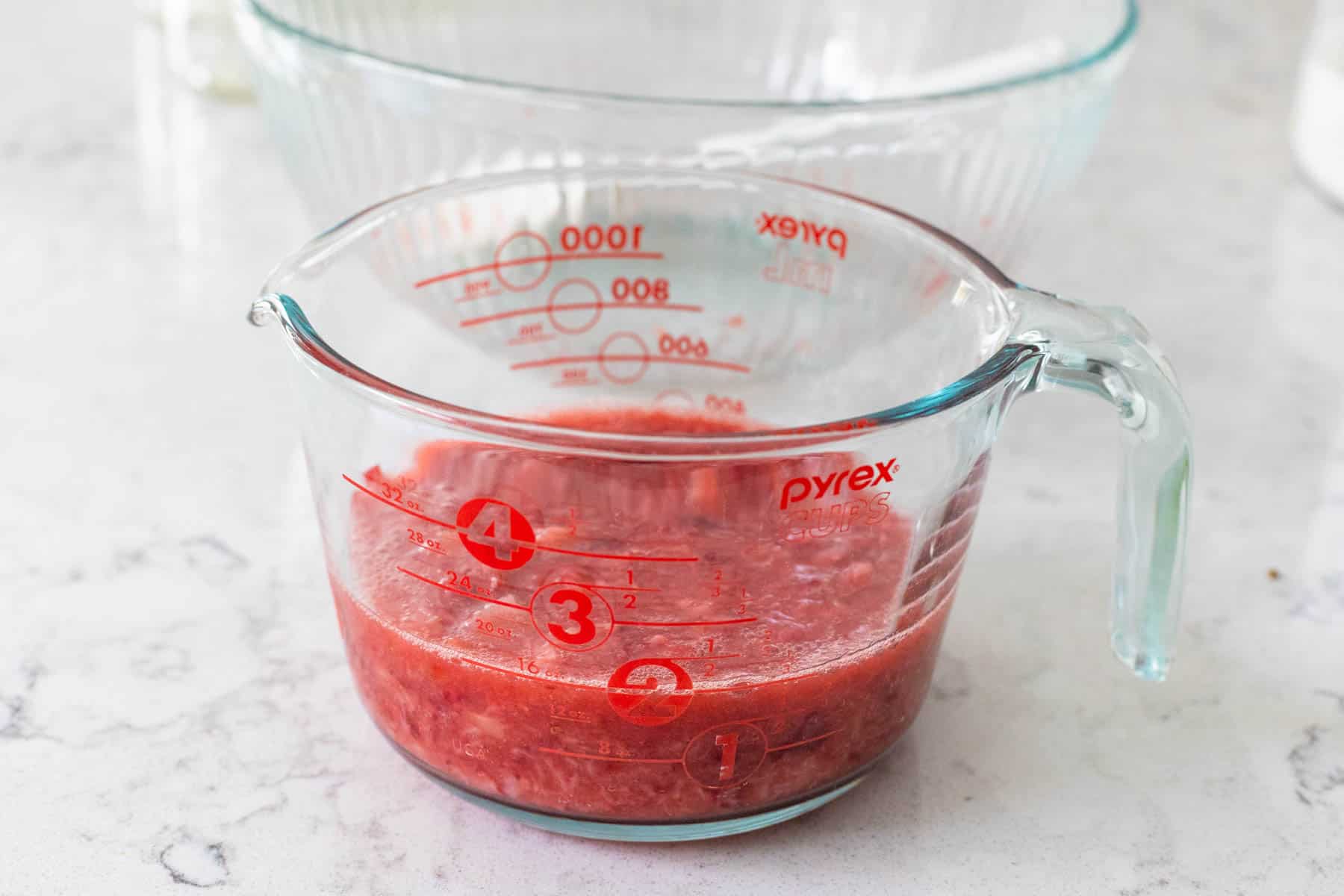 The mashed strawberries have been spooned into a measuring cup.