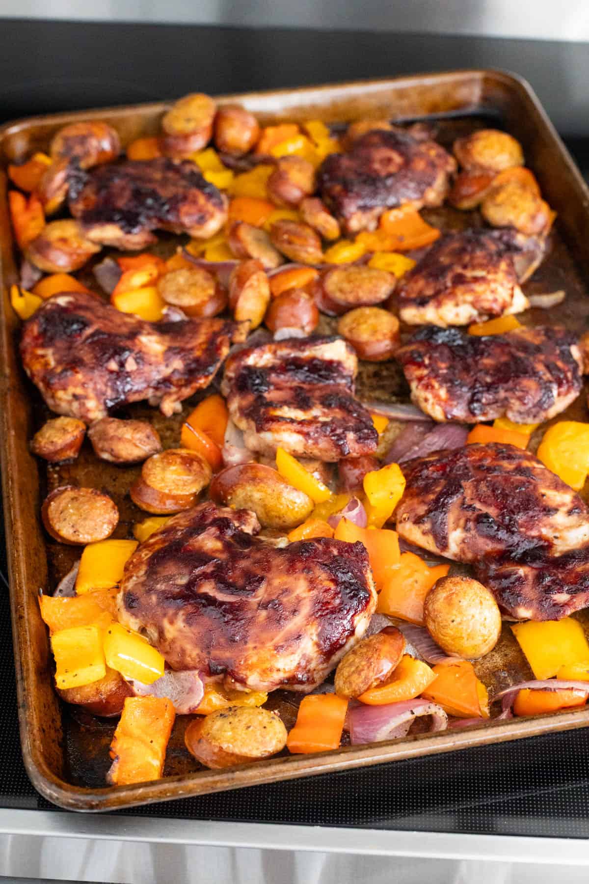The chicken thighs have been placed on top of the sheet pan with sausages and onions. 