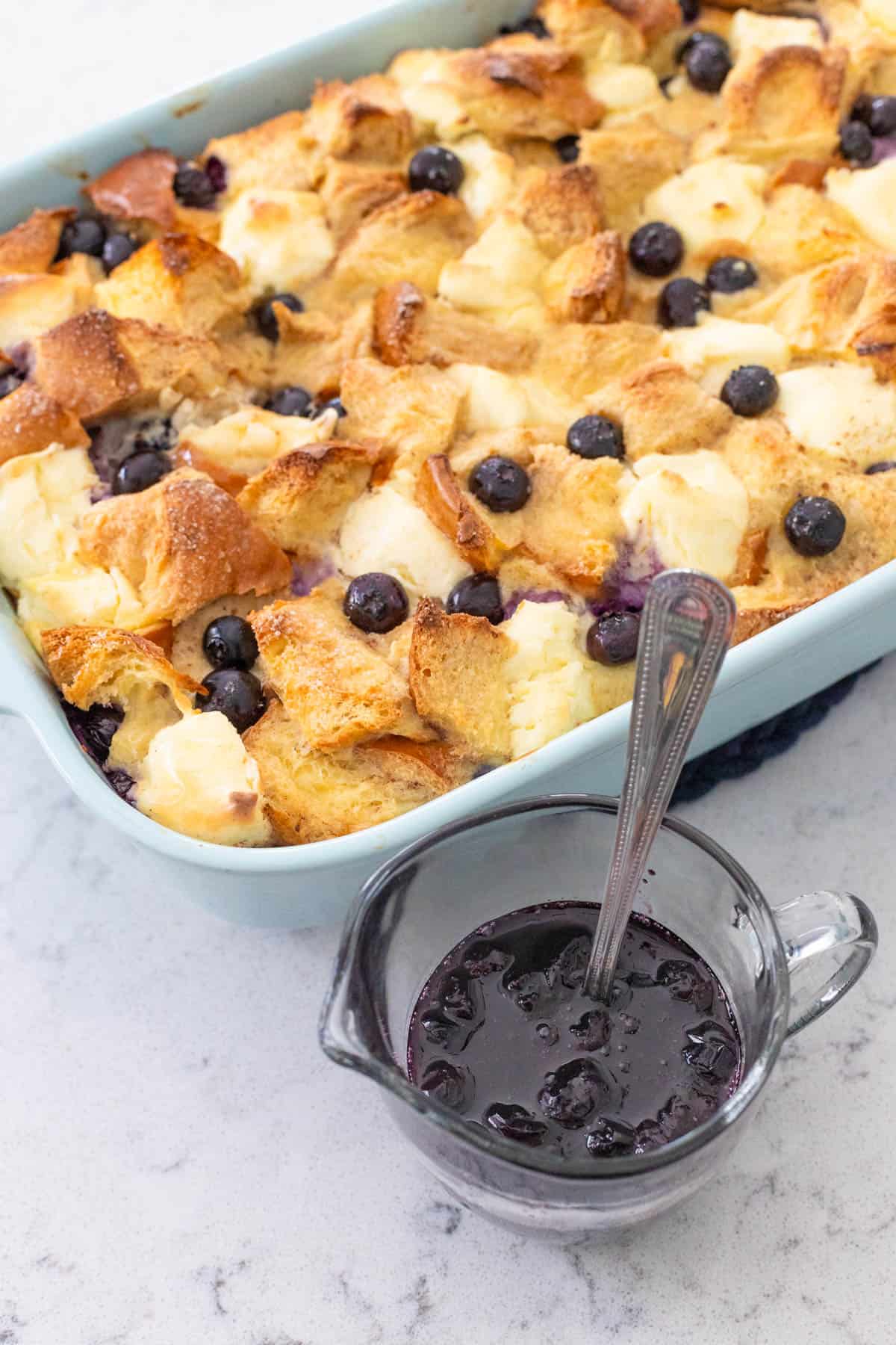 The breakfast casserole has been served with a small pitcher of blueberry maple syrup.