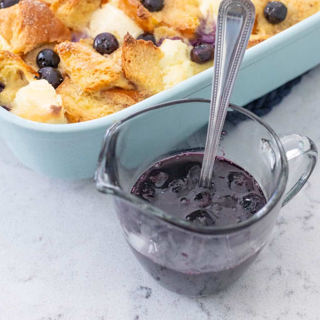 A pitcher of blueberry maple syrup sits next to a breakfast casserole.