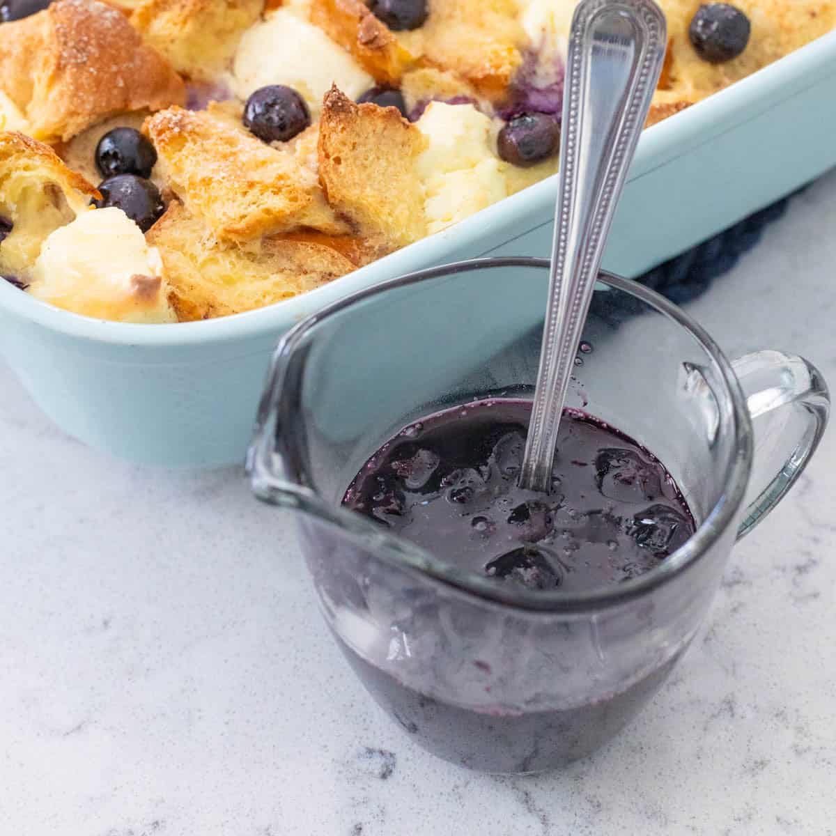 A pitcher of blueberry maple syrup sits next to a breakfast casserole.