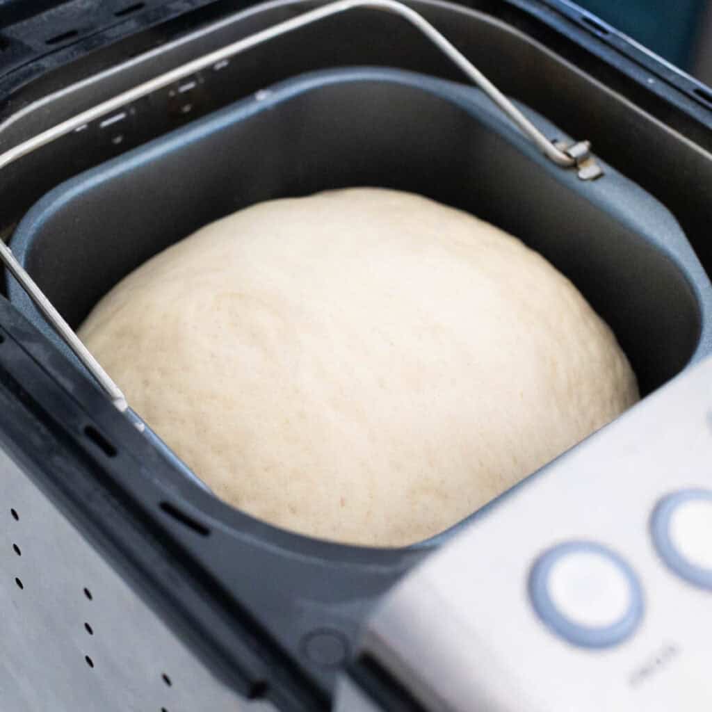 The risen dough is sitting in the bread pan inside the bread machine.
