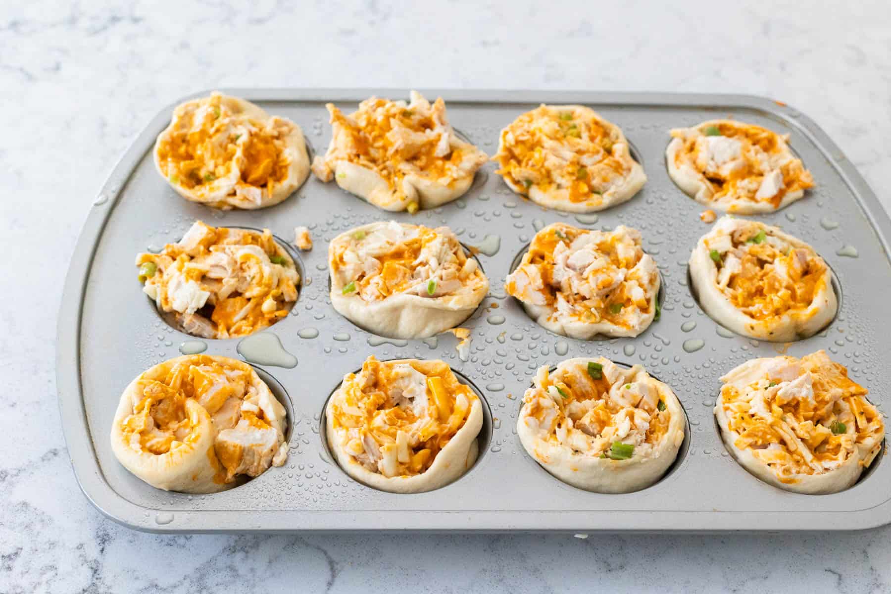 The muffin tin is filled with the prepared buffalo chicken rolls.