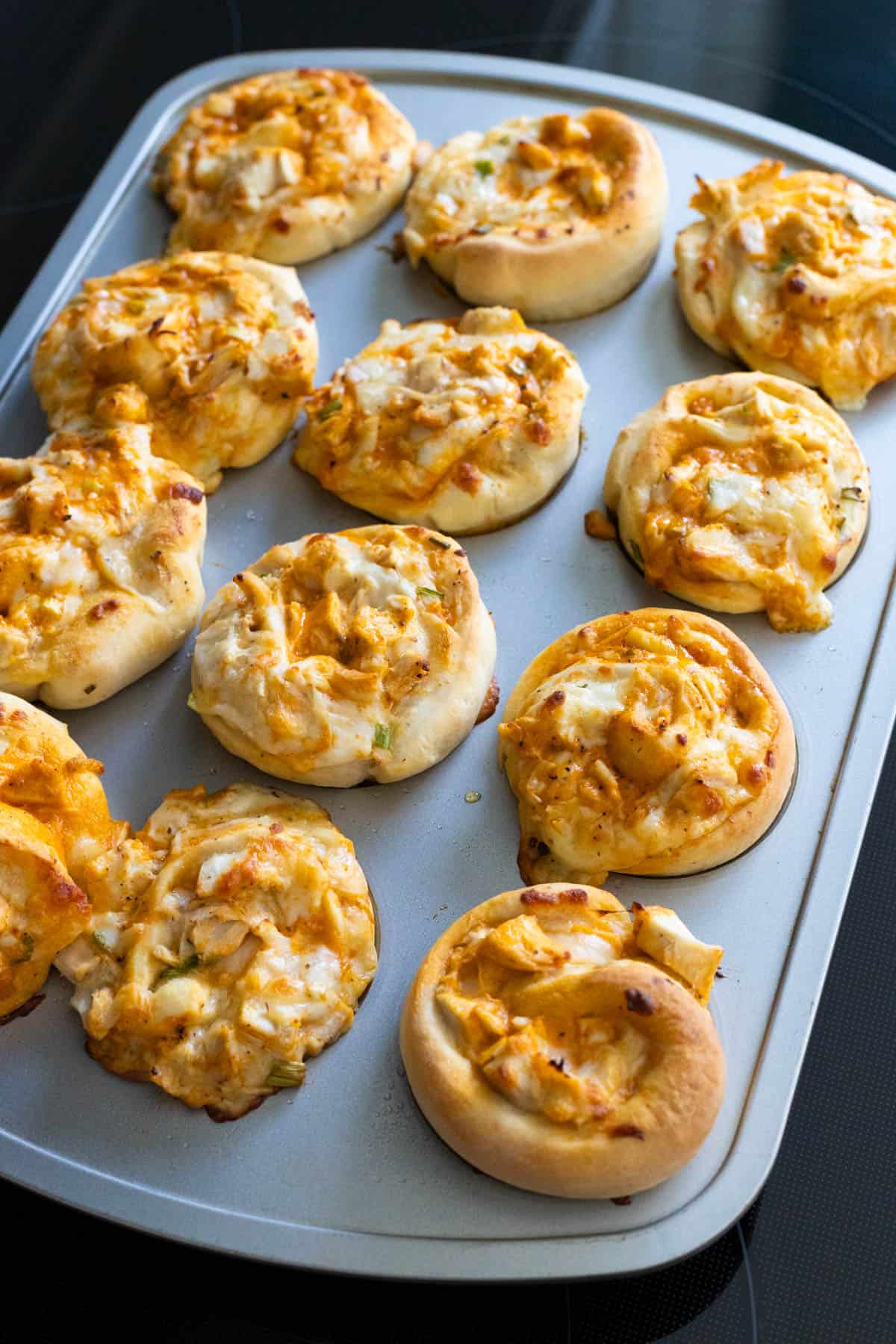 The baked buffalo chicken rolls are cooling in the muffin pan on top of the stove.