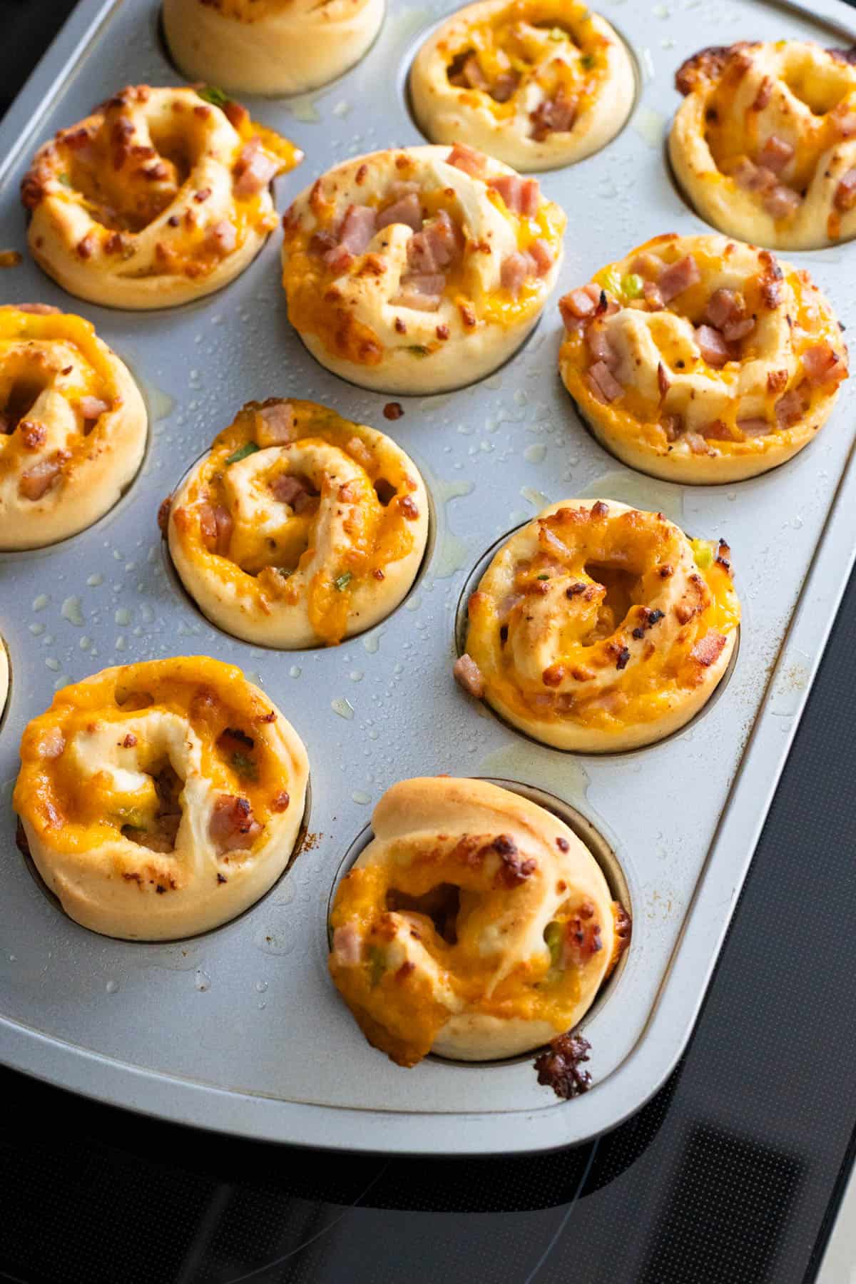 The baked ham and cheese rolls are cooling in the muffin tin on the stovetop.