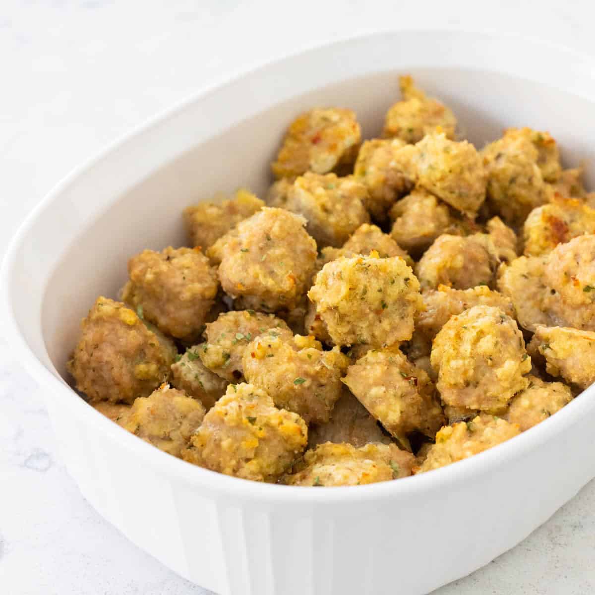A white freezer dish is filled with baked chicken meatballs.
