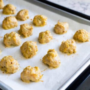 The parchment lined sheet pan is filled with freshly roasted chicken meatballs just out of the oven.