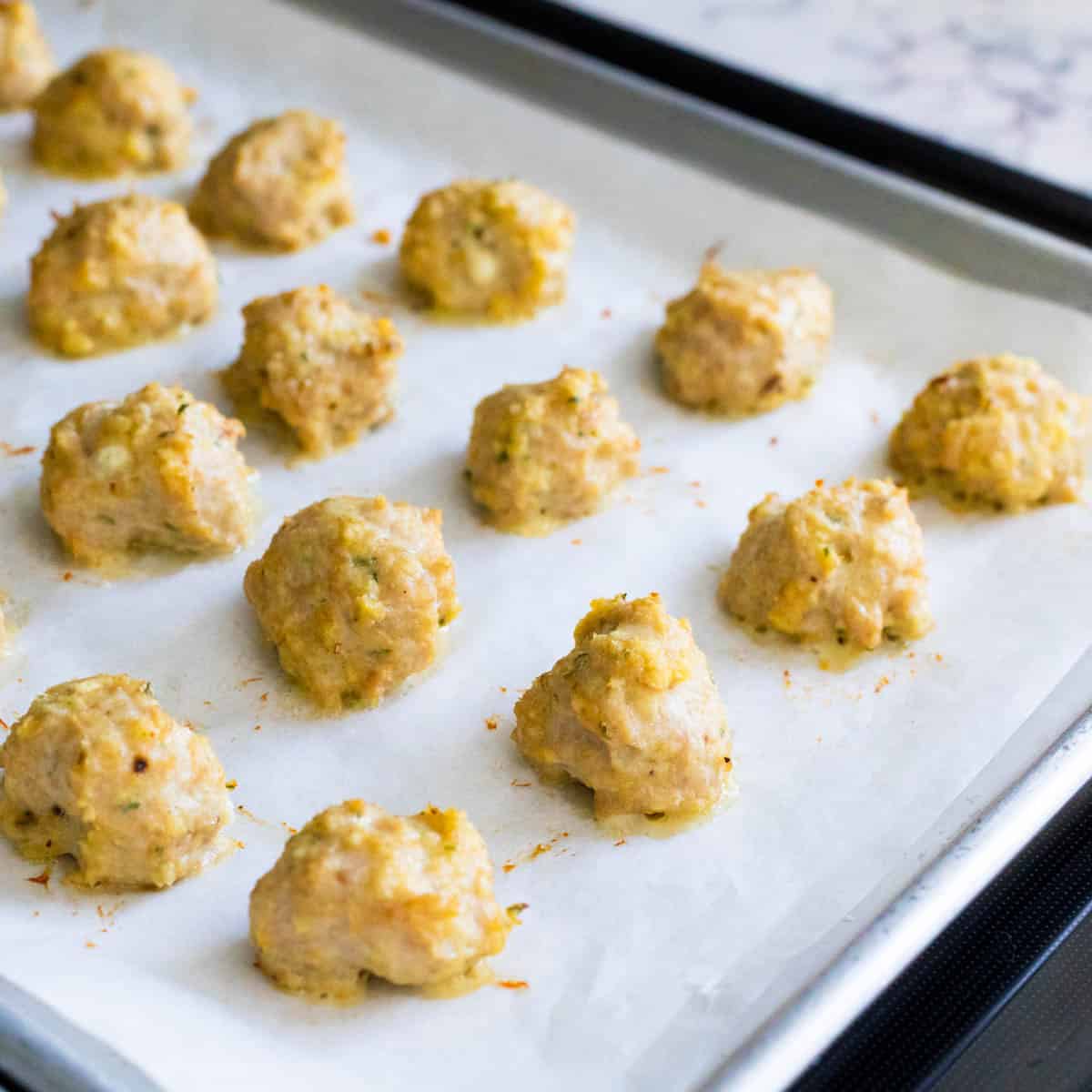 The parchment lined sheet pan is filled with freshly roasted chicken meatballs just out of the oven.
