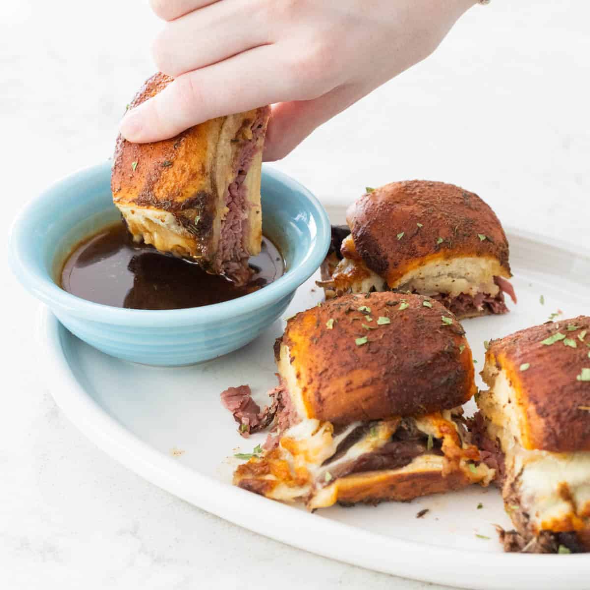 A hand is dipping a French Dip Slider into the cup of dipping sauce. 