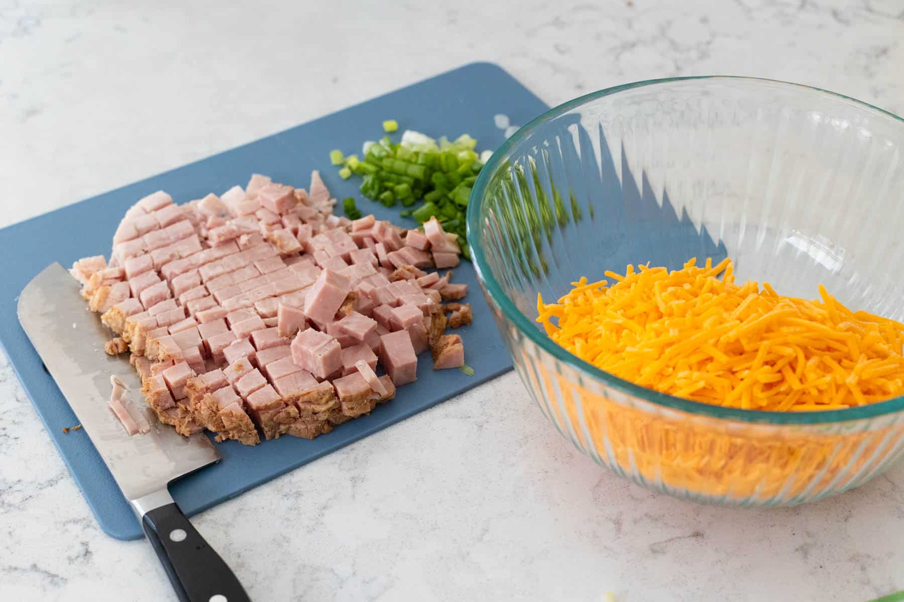 The leftover ham has been diced on a cutting board, and the shredded cheese is in a mixing bowl.