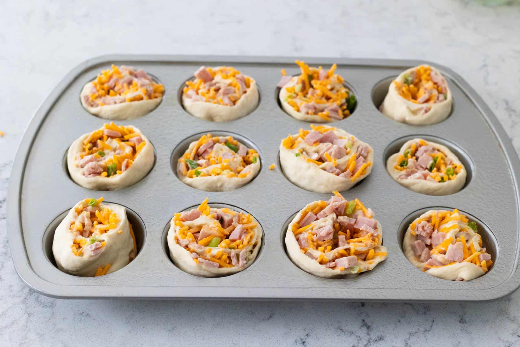 The ham and cheese rolls have been sliced and put into a muffin tin.