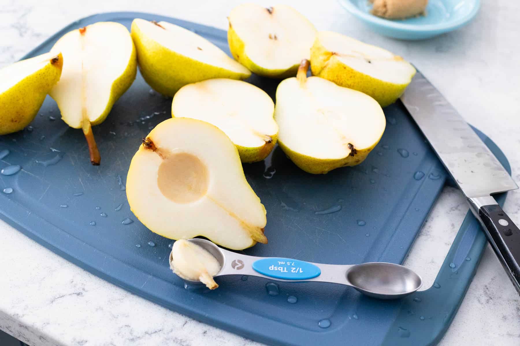 The pears have been sliced in half on a cutting board, and a teaspoon has been used to scoop out the core.