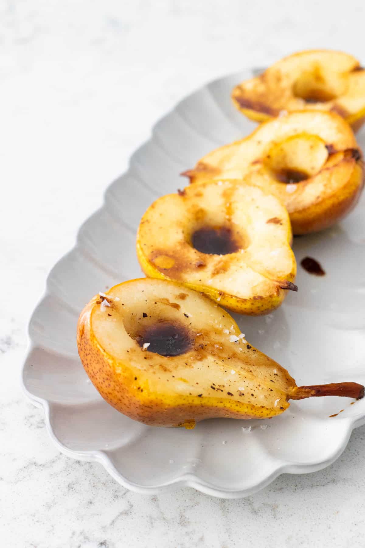 A serving platter has four roasted pear halves lined up.