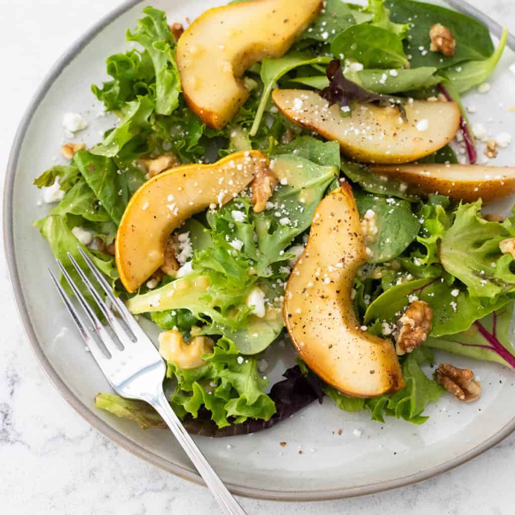 A gray plate is topped with peppery arugula, sliced roasted pears, and a sprinkle of blue cheese and nuts.