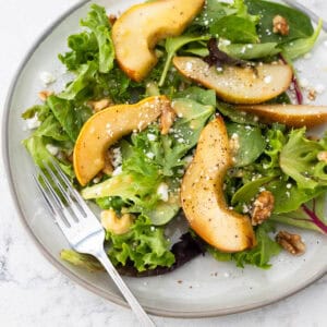 A gray plate is topped with peppery arugula, sliced roasted pears, and a sprinkle of blue cheese and nuts.