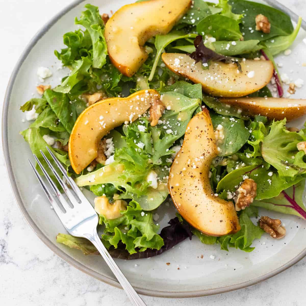 A gray plate is topped with peppery arugula, sliced roasted pears, and a sprinkle of blue cheese and nuts.